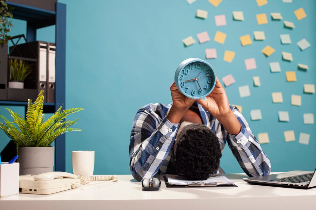 Manager with head on table holds a clock